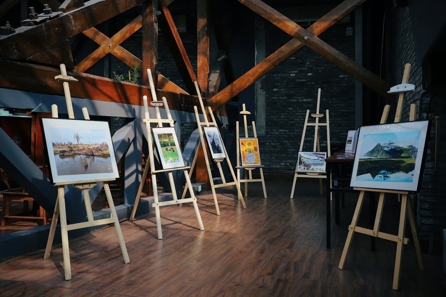 Exposición de arte con obras enmarcadas sobre caballetes de madera.